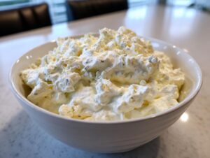 A close-up of chunky, creamy blue cheese dip generously filling a white bowl on a light countertop.