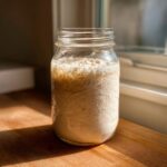 A very active, bubbly sourdough starter filling a glass mason jar, showing significant rise and foam.