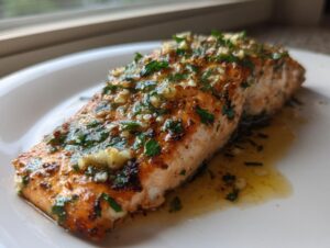 A close-up of a flaky, golden-brown air fryer salmon fillet topped with melted butter, garlic, and fresh parsley.