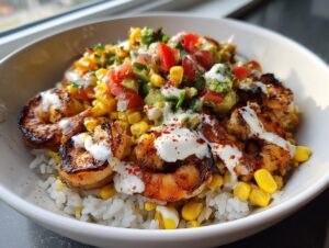 A close-up of a vibrant shrimp bowl featuring grilled shrimp, white rice, corn, pico de gallo, and a creamy white sauce.