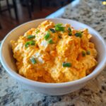 Close-up of creamy, orange-colored boat dip topped with chopped green onions in a white serving bowl.