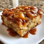 A close-up of a square slice of apple bread pudding generously topped with rich caramel sauce.