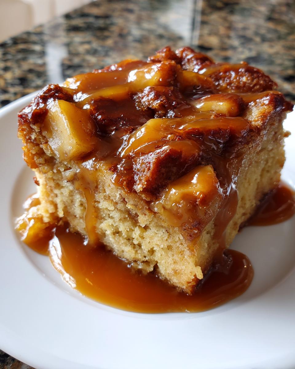 A close-up of a rich slice of apple bread pudding generously topped with warm caramel sauce and baked apples.