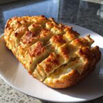A golden-brown loaf of pull-apart cheese bread, scored and baked with melted cheese oozing out.