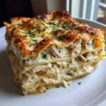 A close-up slice of amazing chicken alfredo lasagna with layers of pasta, creamy sauce, and shredded chicken, topped with melted cheese and parsley.