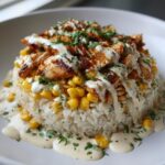 A perfectly plated chicken rice bowl featuring seasoned chicken, corn, white rice, and drizzled with a creamy white sauce and fresh parsley.