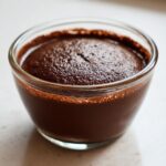 Close-up of rich, dark chocolate pudding freshly made and served in a small clear glass bowl.
