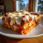 A square slice of baked ziti pasta bake topped with melted mozzarella cheese and rich meat sauce.