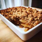 Close-up of a freshly baked pear crisp in a white baking dish, showing bubbling fruit filling and crunchy oat topping.