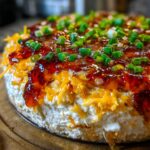 Close-up of a delicious pepper jelly cheese dip layered with cream cheese, shredded cheddar, and topped with sweet jelly and chopped green onions.
