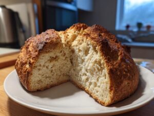 A rustic loaf of freshly baked soda bread, cut open to show the crumb, resting on a white plate.