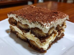 A close-up of a perfect slice of tiramisu recipe showing layers of cream and coffee-soaked ladyfingers, topped with cocoa powder.