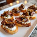 Close-up of several steak crostini appetizers topped with rare steak, creamy cheese, and caramelized onions.