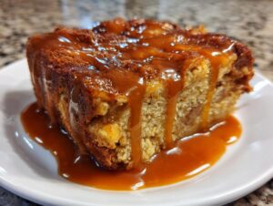 A close-up of a moist slice of apple bread pudding generously drizzled with thick caramel sauce.