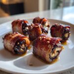 Five crispy, glazed bacon-wrapped stuffed dates glistening with syrup on a white plate.