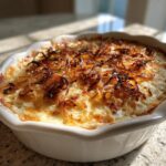Close-up of a baked caramelized onion dip in a white dish, topped generously with crispy fried onions.