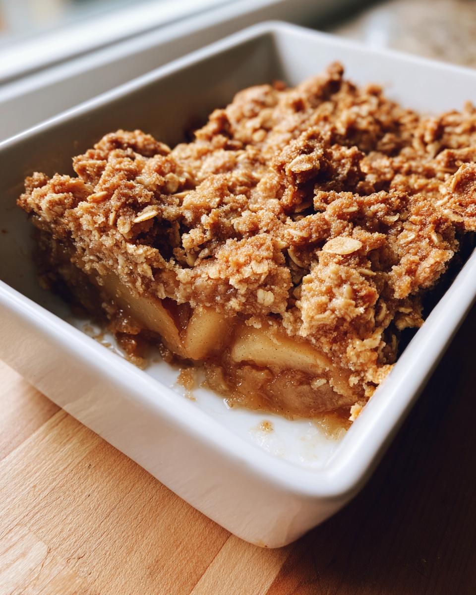 A close-up view of a golden brown, crumbly topping over soft, spiced fruit in a white baking dish, showcasing the delicious pear crisp.