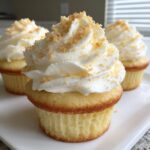 A close-up of three moist banana pudding cupcakes topped with swirled white frosting and crushed wafer crumbs.
