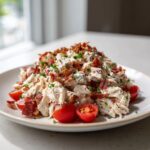 A mound of creamy blt chicken salad topped generously with crispy bacon bits and fresh parsley, served with cherry tomatoes.