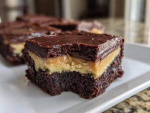 A close-up view of a single, rich buckeye brownies square showing the three distinct layers: brownie base, peanut butter filling, and chocolate ganache topping.