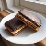Two homemade buckeye graham crackers stacked on a white plate, featuring chocolate topping and peanut butter filling.