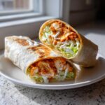 Two halves of a perfectly grilled buffalo chicken wrap, showing shredded chicken, lettuce, and ranch drizzle.