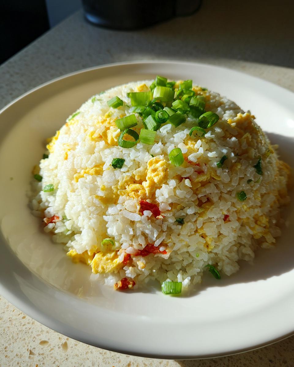 A mound of white cauliflower rice mixed with scrambled egg and topped with fresh green scallions, served on a white plate.
