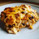 A close-up of a serving of cheesy chicken burrito bake showing shredded chicken, rice, and black beans under melted cheddar.