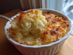 A spoonful of creamy, cheesy potato comfort being lifted from a white ramekin showing a deeply browned, crispy cheese topping.