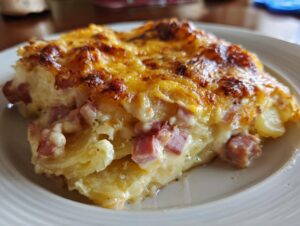 A close-up of a cheesy, baked slice of scalloped potatoes and ham served on a white plate.