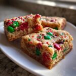 Close-up of three thick, chewy christmas cookie bars topped with red and green M&Ms and festive sprinkles.