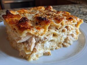 A thick, square slice of creamy chicken alfredo lasagna showing layers of pasta, shredded chicken, and a bubbly, browned cheese top.
