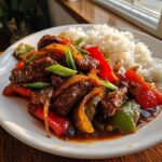 A plate of savory chinese pepper steak stir-fry with colorful bell peppers, onions, and a side of fluffy white rice.