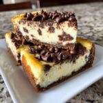 Two stacked slices of rich chocolate chip cheesecake bars topped with melted chocolate and mini chocolate chips.