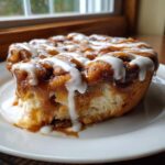 A close-up of a slice of cinnamon roll apple pie, dripping with white icing and caramel sauce.