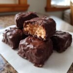 A stack of homemade chocolate-covered bars, one with a bite taken out showing the coconut filling of this cool whip candy.