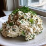 A mound of creamy cottage cheese chicken salad mixed with celery and topped with fresh dill, served on a white plate.