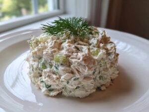 A mound of creamy cottage cheese chicken salad, mixed with celery and topped with fresh dill, served on a white plate.