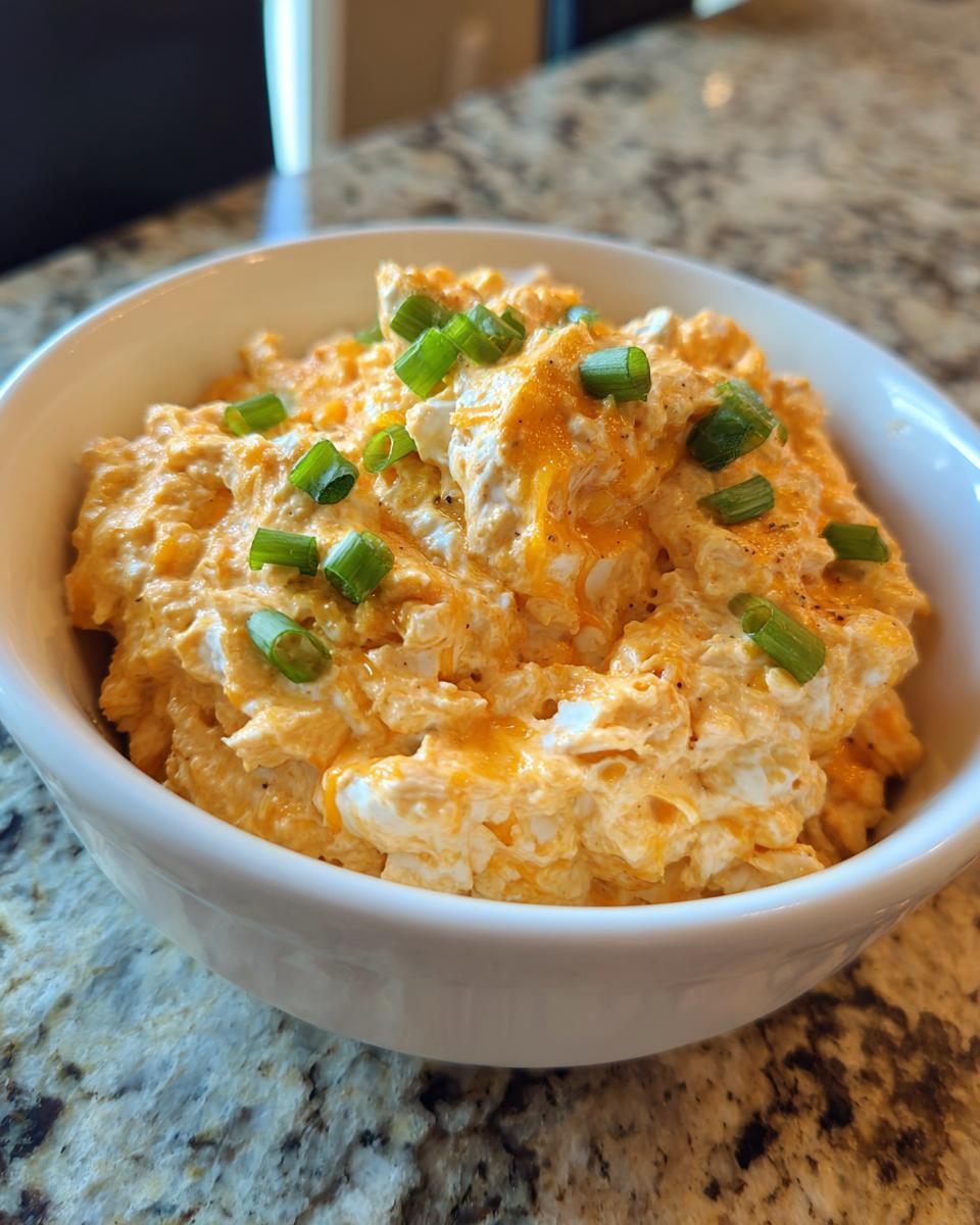 Close-up of creamy, orange-tinted boat dip topped with shredded cheese and chopped green onions in a white bowl.