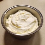 A close-up of thick, white, creamy mixture, likely the base for horseradish sauce, in a small stainless steel bowl.