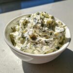 A close-up of thick, creamy blue cheese dip mixed with green herbs served in a small white bowl.