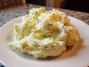 A generous serving of creamy Boursin mashed potatoes speckled with green chives on a white plate.
