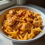 Close-up of a white bowl filled with creamy cajun chicken pasta, featuring wide noodles and chunks of chicken coated in a rich, orange sauce.