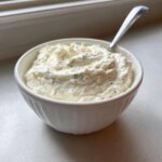 A white bowl filled with thick, textured creamy horseradish sauce mixed with visible green herbs.