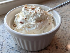 A white ramekin filled with fluffy, whipped creamy horseradish sauce, topped with small brown specks, with a spoon resting inside.