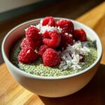 A close-up of creamy matcha chia pudding topped with fresh raspberries and shredded coconut.