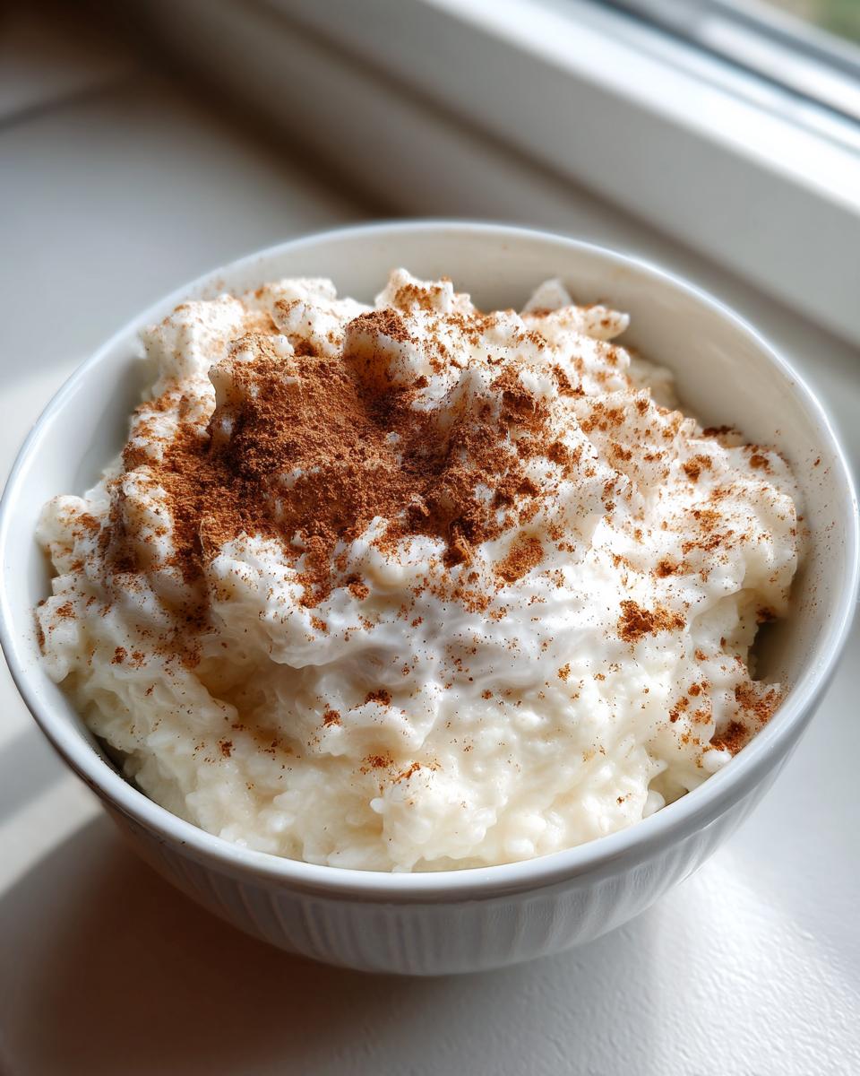 Close-up of creamy rice pudding in a white bowl, generously topped with ground cinnamon.
