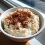 Close-up of creamy rice pudding served in a white bowl, generously dusted with cinnamon.
