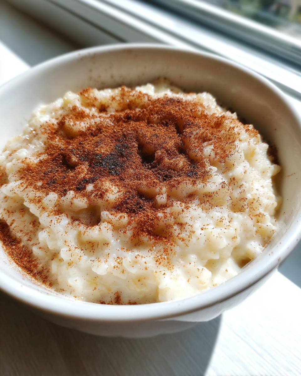 A close-up of creamy rice pudding in a white bowl, generously dusted with cinnamon powder.