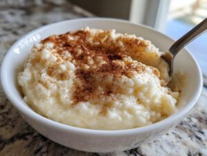 Close-up of a white bowl filled with creamy rice pudding recipe, topped generously with ground cinnamon.